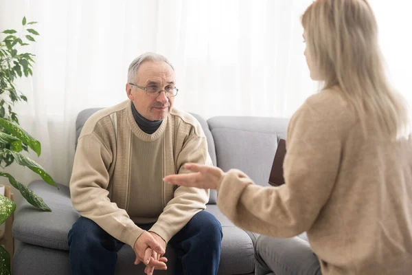 stock image Senior man patient and young woman caregiver medical worker in uniform hold clipboard noting personal information talking listens client telling about health complaints, care support nursing concept