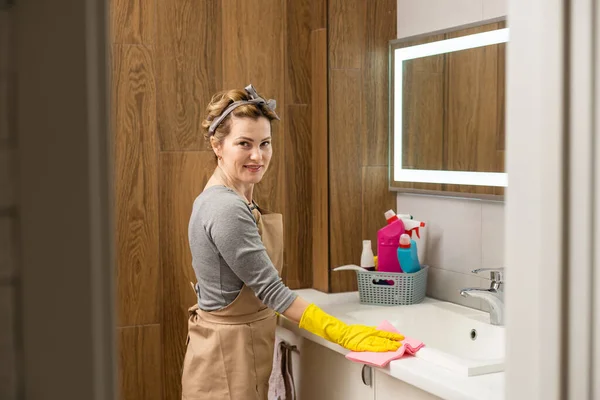Young woman doing house chores. Woman holding cleaning tools. Woman wearing rubber protective yellow gloves, holding rag and spray bottle detergent. Its never too late to spring clean.