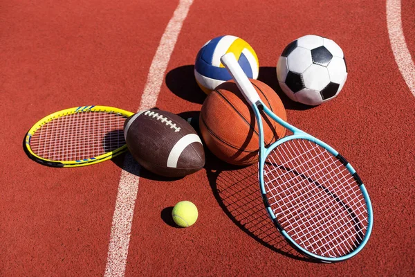A variety of sports equipment including an american football, a soccer ball, a tennis racket, a tennis ball, and a basketball.