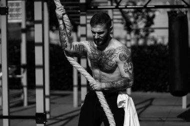 Kaslı yakışıklı adam şehir merkezindeki sokak sporları sahasındaki makinelerde üst vücut eğitimi veriyor.