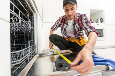 Mutfakta alet çantasıyla bulaşık makinesini inceleyen bir tamirci. Yüksek kalite fotoğraf