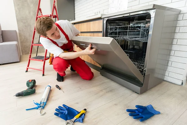 Full length of repairman repairing dishwasher with screwdriver in kitchen