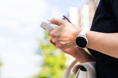 İş kadını bileğine ses kontrolü olan akıllı bir saat takıyor ve güneşli bir günde cep telefonunu kullanıyor. Yüksek kalite fotoğraf