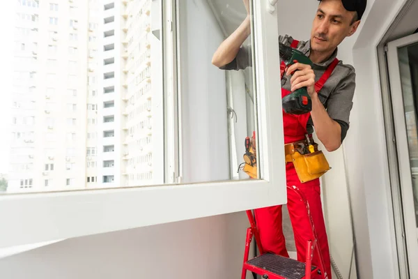 Construction worker repairing plastic window with electric screwdriver indoors. High quality photo