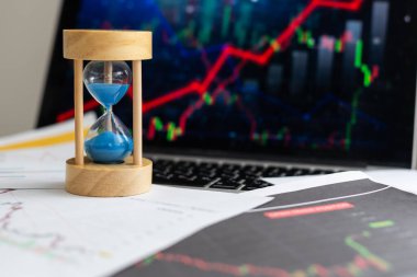 Finansal tablolar ve grafiklerin arka planında kum saati ve yığınla altın para var. Yüksek kalite fotoğraf