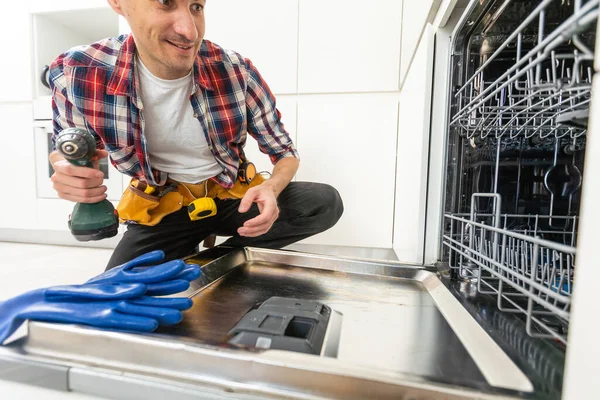 Worker using screwdriver to repair dishwasher at home stock photo. High quality photo