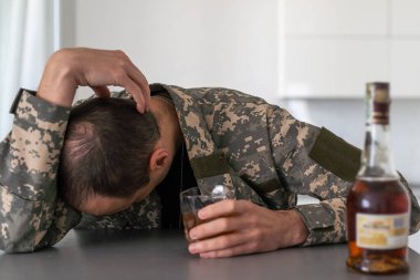 Kamuflajlı bir adam ordudan döndükten sonra depresyona girer. Alkol ve uyuşturucu hapları kullanıyor. Ağır anılar yüzünden acı çekiyor. Masanın üzerinde bir silah var. Yüksek kalite fotoğraf