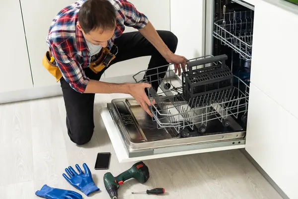 Professional worker repairing the dishwasher in the kitchen. High quality photo