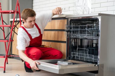 Üniformalı teknisyen ya da işçi mutfak mobilyalarına bulaşık makinesi yerleştiriyor. Tamirci bulaşık makinesini tamir ederken işçi kıyafeti giyer. Koruyucu eldivenlerde uzman Bulaşık makinesini tamir eder.