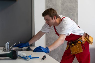 Erkek tesisatçı müşteri evinde lavabo musluğu tamir ediyor. Tamirci ya da tamirci müşteri mutfağında boru hattını tamir eder. Kaliteli tesisat şirketi servisi. Bakım ve ev yardımı kavramı.