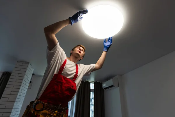 Electrician at work. Service for the repair of electrical wiring and replacement of ceiling lamps. A builder is installing a loft-style wooden ceiling. Rent-a-gent helps with the housework.