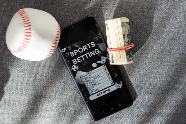 Business and sport concept. Ball and smartphone with bet application on dollar bills and keyboard. High quality photo