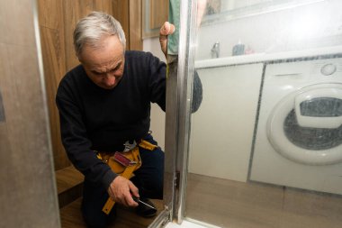 an elderly man is repairing a shower cabin.