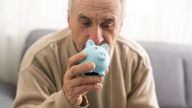 an elderly man is holding a piggy bank.