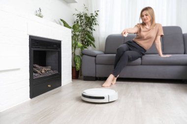 Dinlenen kadının olduğu koltuğun yanındaki modern robot elektrikli süpürge.