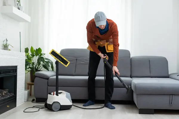 Dry cleaners man employee removing dirt from furniture in flat, closeup, vacuum clean sofa with professional equipment
