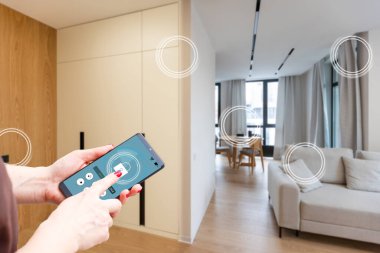Mobil uygulamada ev sıcaklığı, güvenlik ve çevre kontrolü. Kadın elinde akıllı telefon. Arka planda oturma odası.