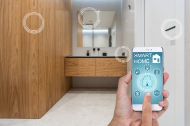 Elinde akıllı telefon tutan ve evinde güvenlik uygulaması olan genç bir kadın. Ev güvenliğini mobil bir cihazdan kontrol etme ve yönetme kavramı.