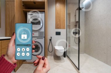 Akıllı ev otomasyon uygulaması arka planda ev içi olan kadın eliyle akıllı telefondan tutulan.