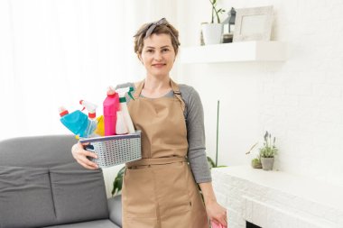 Ev işleri yapan genç bir kadın. Elinde temizlik aletleri olan kadın. Plastik koruyucu sarı eldivenler giyen, elinde bez parçası ve sprey deterjan tutan bir kadın. Bahar temizliği için asla geç değildir..