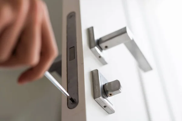 A locksmith is repairing an interior door lock. Close-up of male hands repairing or replacing an entrance door lock with a hex screwdriver. High quality photo