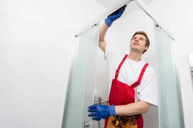 Genç adam banyoda duş kabinin kapısı tamiri