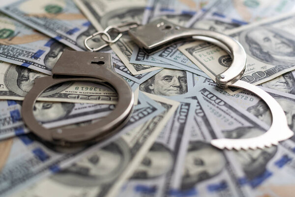 Пара наручников крупным планом на фоне долларовых банкнот. Коррупционная проблема в мире. Высокое качество фото