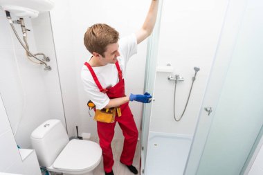 Üniformalı tamirciler banyodaki modern duş kabinini ölçüyorlar..