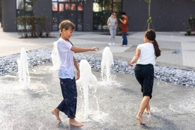 Sıcak bir günde, çocuklar koşar ve şehir çeşmesinde eğlenirler. Boş zaman konsepti. Yaz tatili. Mutlu çocukluk. Yüksek kalite fotoğraf