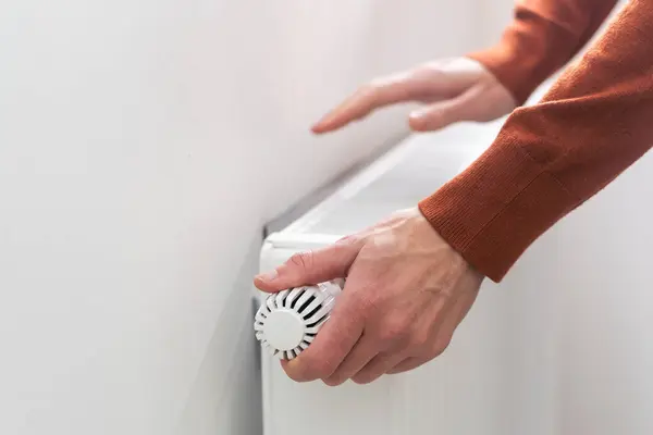 Close-up of a mans hand raising the temperature of a heating battery. Temperature control of the radiator of the water heating system in the living room.