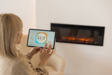 Arka planda şöminesi olan rahat bir oturma odasında dijital tableti tutmak. akıllı ev uygulaması.