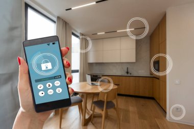 Mobil uygulamada ev sıcaklığı, güvenlik ve çevre kontrolü. Kadın elinde akıllı telefon. Arka planda oturma odası.