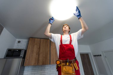 Genç adam mutfaktaki merdivene lamba yerleştiriyor..