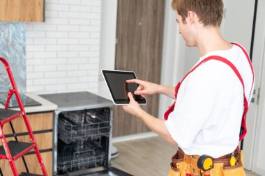 Portrait Of Male Technician Repairing Dishwasher In Kitchen using digital tablet