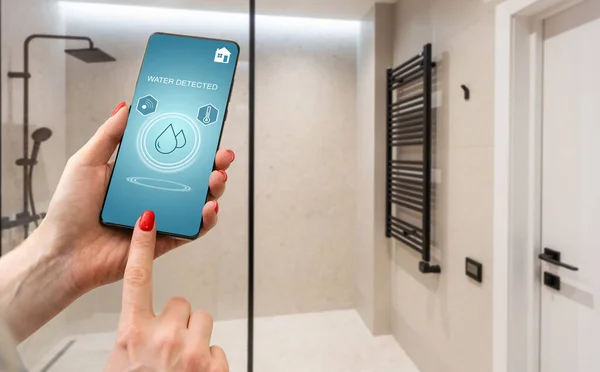 Hand holding smart phone with home control application with water detected, Smart home concept