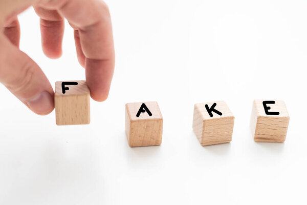 Слово "FAKE" пишется деревянными буквенными плитками на белом фоне. Высокое качество фото