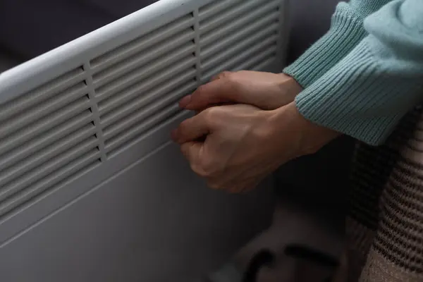 Woman warming hands near heater indoors, closeup.