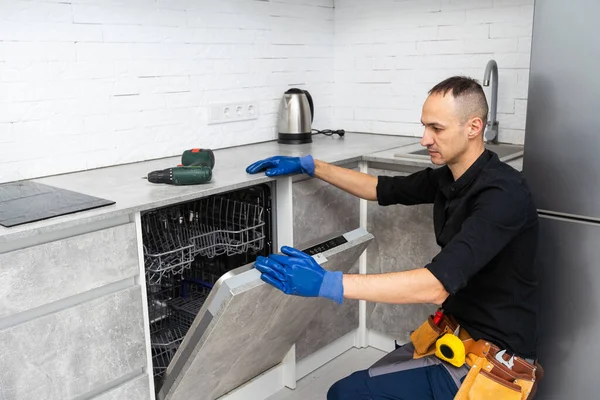 A plumber repairs a dishwasher in a kitchen room. Plumbing services. . High quality photo