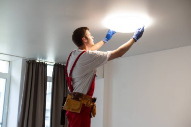 Bir elektrikçi tavana LED spot ışıkları kuruyor.