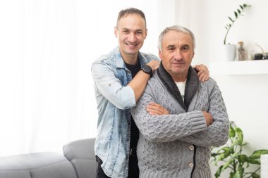 Yakışıklı, gülümseyen yetişkin bir adam yaşlı, olgun bir babaya sarılıyor, kameraya bakıyor. Mutluluk, sevgi ve ilgi. İki nesildir aile portresi çekiliyor. Babalar Günü konsepti. Yüksek kalite fotoğraf