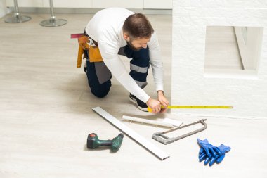 Etek tahtalarının kurulumu, ana yapıştırıcılar duvarın dış köşesine zemin silindirleri, eller.