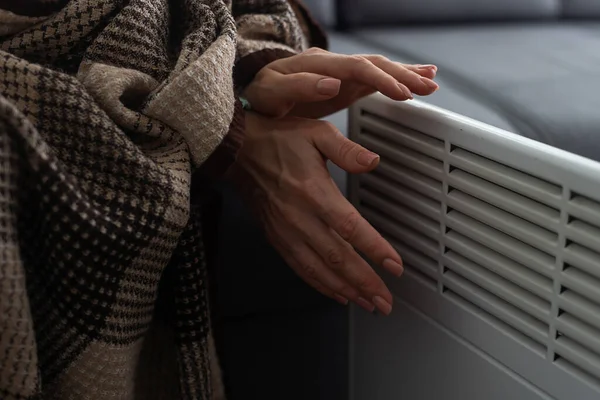 Woman warming hands near electric heater at home, closeup.