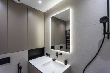 Banyo gri ve beyaz zemin ile modern bir tarzda. Aydınlık lambaları, Masa üstü ahşap çekmece ve lavabo, banyo duş ve cam bölme, havlu askısı ile bir askı ile büyük bir ayna.