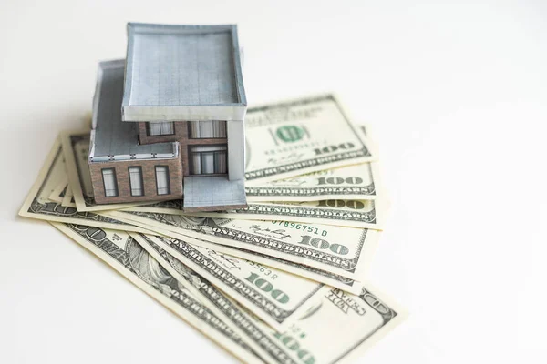 A small house lies on a fan of hundred dollar bills. The keys to the purchased house. Reduced copy of the house on a white background. High quality photo