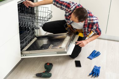 Bulaşık makinelerinin tamiri. Tamirci mutfakta bulaşık makinesini tamir ediyor. Yüksek kalite fotoğraf