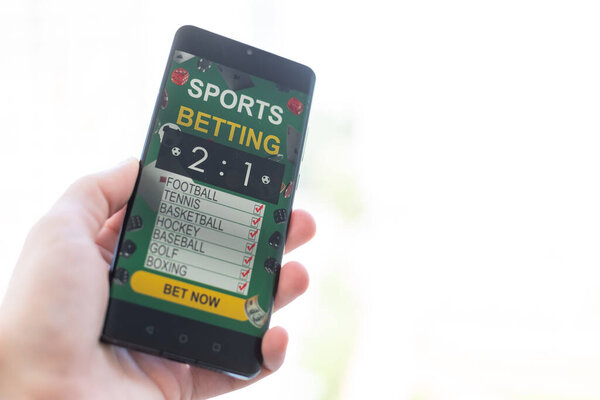 Man betting on sports using smartphone and laptop at table, closeup. Bookmaker websites on displays. High quality photo