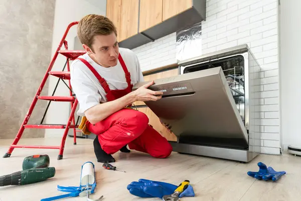 Concept maintenance service of home appliances. Worker cleans filter in the dishwasher. Male repairman checking food residue filters.