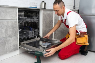 Genç Tamirci Bulaşık makinesini elektrikli matkapla tamir ediyor. Yüksek kalite fotoğraf
