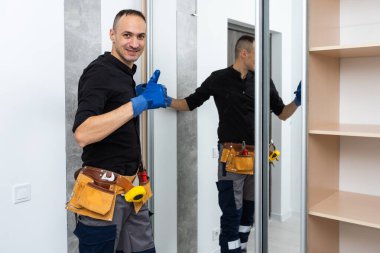 İşçi köşede aynalı kapılar yerleştiriyor. Odada gardırop kayıyor. Yüksek kalite fotoğraf