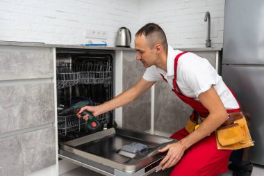 Mutfakta alet çantasıyla bulaşık makinesini inceleyen bir tamirci. Yüksek kalite fotoğraf